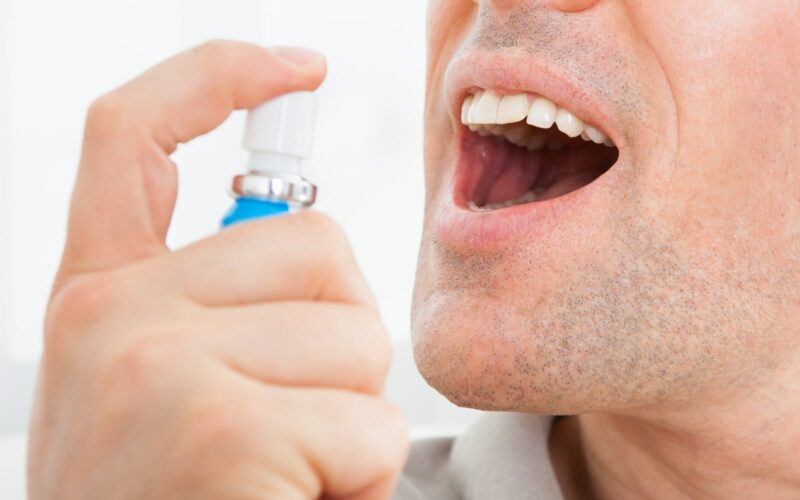 Man showing teeth and using inhaler